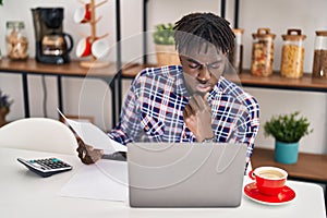 African american man using laptop reading document accounting at home