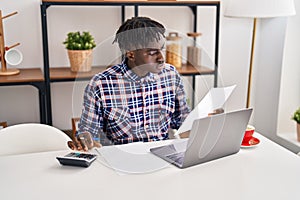 African american man using laptop reading document accounting at home