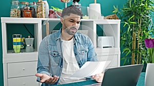 African american man using laptop reading document looking upset at dinning room