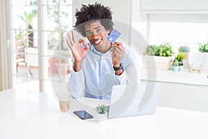 African American man using laptop and shopping online with credit card doing ok sign with fingers, excellent symbol