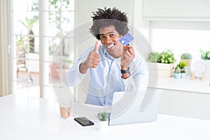 African American man using laptop and shopping online with credit card happy with big smile doing ok sign, thumb up with fingers,