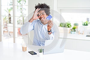 African American man using laptop and shopping online with credit card with happy face smiling doing ok sign with hand on eye