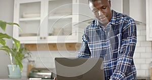 African american man using laptop and talking on smartphone in kitchen at home, slow motion