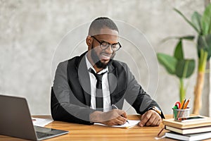 African American man using laptop writing in notebook