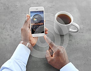 African-American man using weather forecast app on smartphone at table