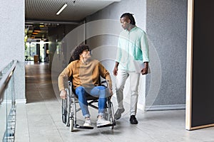 African American man walking beside biracial man in wheelchair in a modern business office