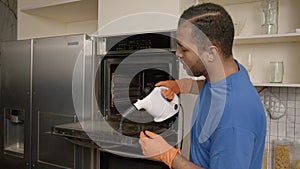 African American man washing kitchen oven from grease using steam cleaner