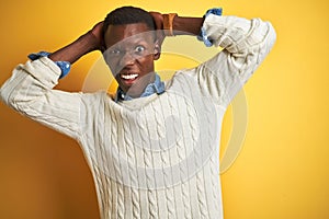 African american man wearing denim shirt and white sweater over isolated yellow background Crazy and scared with hands on head,