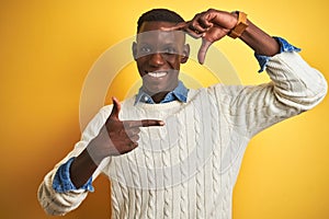 African american man wearing denim shirt and white sweater over  yellow background smiling making frame with hands and