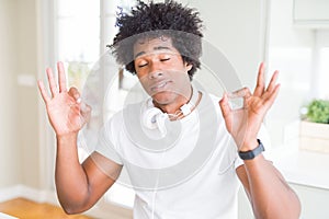 African American man wearing headphones listening to music relax and smiling with eyes closed doing meditation gesture with