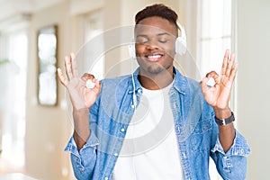 African american man wearing headphones listening to music relax and smiling with eyes closed doing meditation gesture with