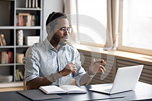 African American man wearing headphones speaking, using laptop