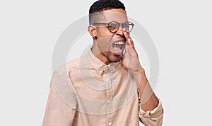 African American man wearing round eyewear, beige shirt and wide opened mouth screaming with great fear and anger. Furious dark-