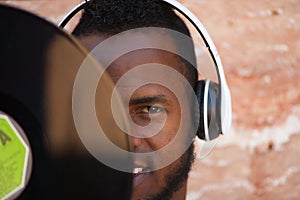 African american man with white headphones holding a vinyl record in his hand and covering part of his face