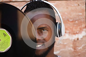 African american man with white headphones holding a vinyl record in his hand and covering part of his face