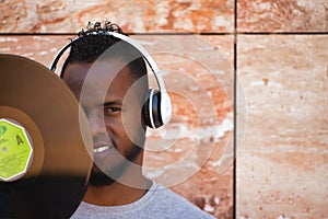 African american man with white headphones holding a vinyl record in his hand and covering part of his face