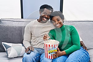 African american man and woman couple watching movie eating popcorn at home