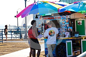 An African American man and woman standing in front of a photo vender on the pier surrounded by colorful umbrellas