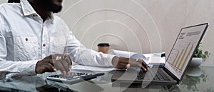 African American man working with laptop computer and using calculator, making financial audit, reviewing bills tax and