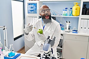 African american man working at scientist laboratory with apple angry and mad screaming frustrated and furious, shouting with