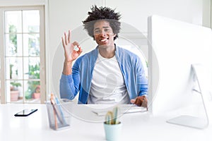 African American man working using computer doing ok sign with fingers, excellent symbol