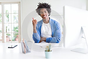 African American man working using computer happy with big smile doing ok sign, thumb up with fingers, excellent sign