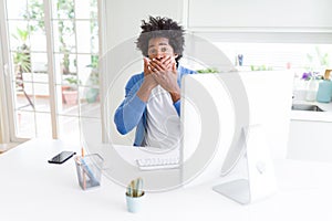 African American man working using computer shocked covering mouth with hands for mistake