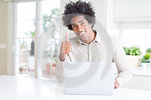 African American man working using laptop happy with big smile doing ok sign, thumb up with fingers, excellent sign