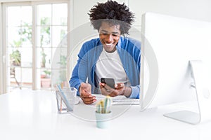 African American man working using smartphone and computer with a happy face standing and smiling with a confident smile showing