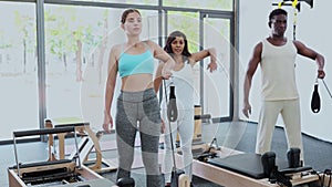 African-american man and young european woman exercising with pilates reformers. Latin woman instructor assisting them