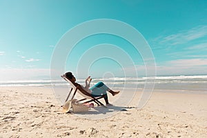 African american mature woman using digital tablet relaxing on deckchair at beach against sky