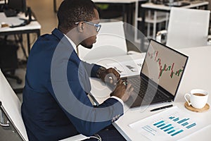 African American men in a business suit are working on a laptop studying stock market charts and technical analysis.
