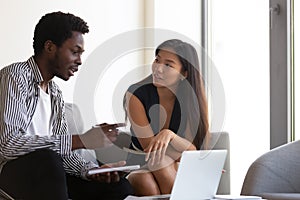 African American mentor training Asian intern, using laptop