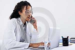 African american mid adult woman talking over smart phone and using laptop on desk, copy space
