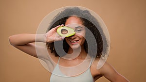 African American model beautiful attractive woman girl in beige ad advertise background holding fresh avocado near face