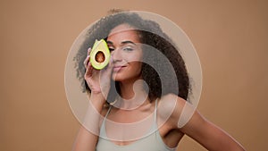 African American model beautiful attractive woman girl in beige ad advertise background holding fresh avocado near face