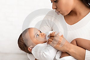 African American Mom Feeding Baby Giving Bottle With Milk Indoors