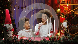 African American mom and little daughter burning white candles with wow delight emotions. Woman and girl sitting near