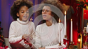 African American mom and little daughter in white sweaters light candles with wow delight emotions. Happy family