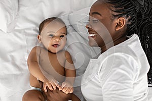 African American mom lying in bed with her laughing baby