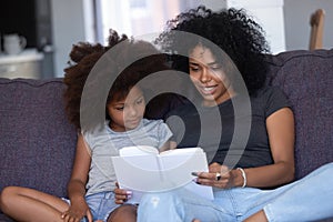 African american mom reading book to little daughter at home