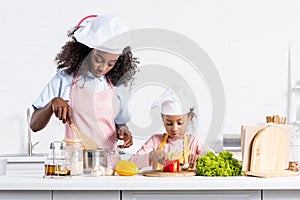 african american mother and daughter in chef hats cooking