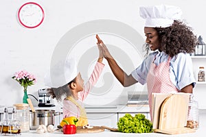 african american mother and daughter in chef hats cooking and giving high five