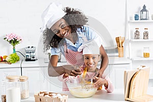 african american mother and daughter in chef hats mixing dough with whisk