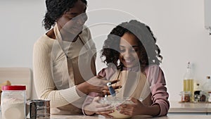 African american mother and daughter cooking dough together at kitchen, woman taking daugh and messing girl's nose