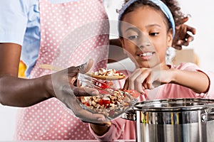 african american mother and daughter putting ingredientes in saucepan photo