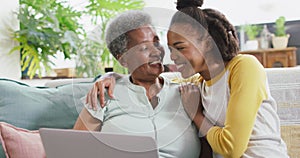 African american mother and daughter smiling while using laptop together at home