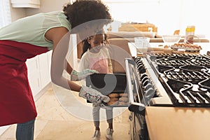 African American mother and daughter taking cookies from the oven