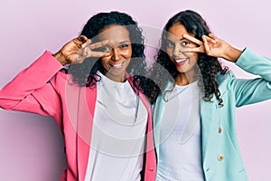 African american mother and daughter wearing business style doing peace symbol with fingers over face, smiling cheerful showing