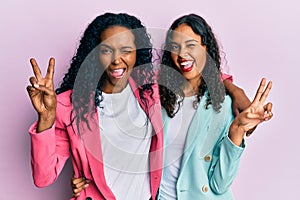 African american mother and daughter wearing business style smiling with happy face winking at the camera doing victory sign with